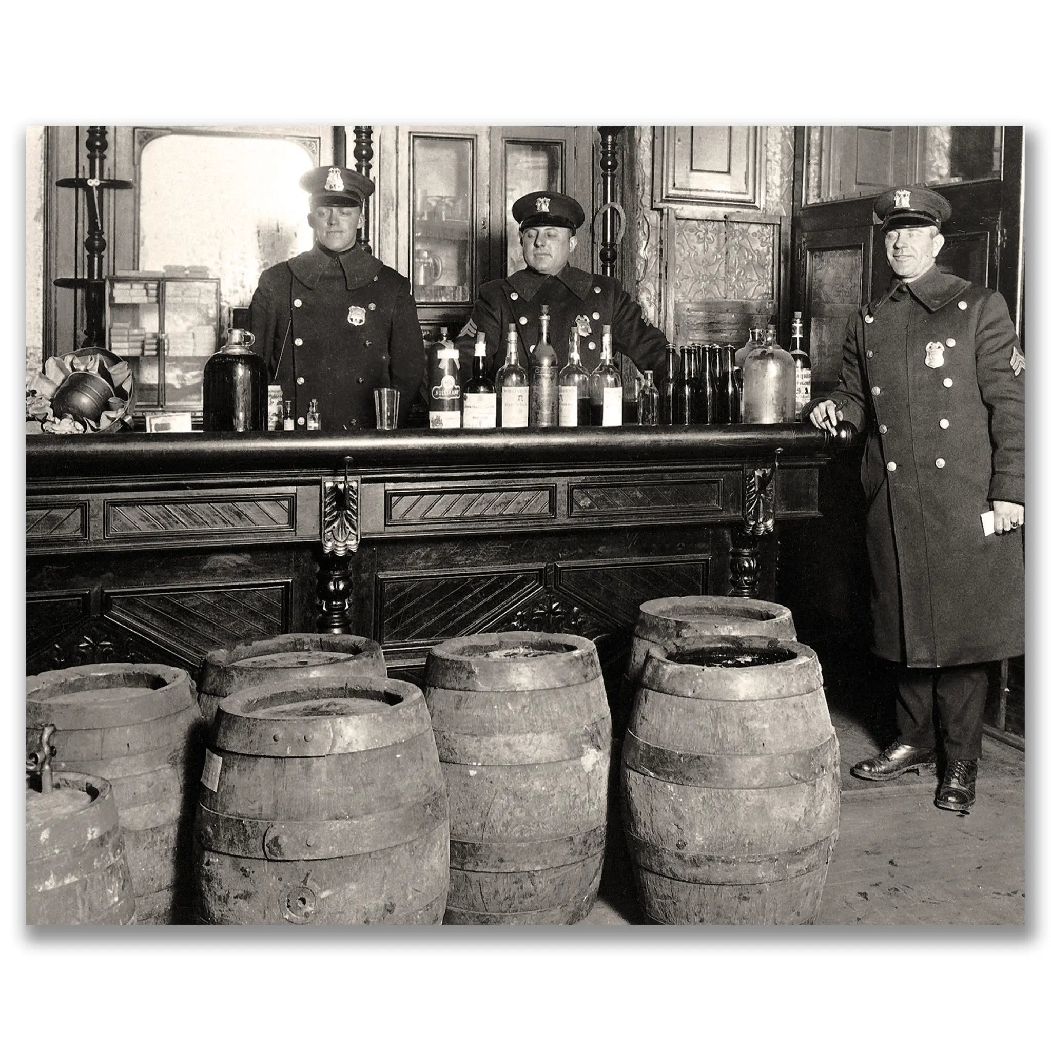 Historic prohibition police raid evidence photograph showing three uniformed officers with massive alcohol seizure behind ornate bar with confiscated barrels