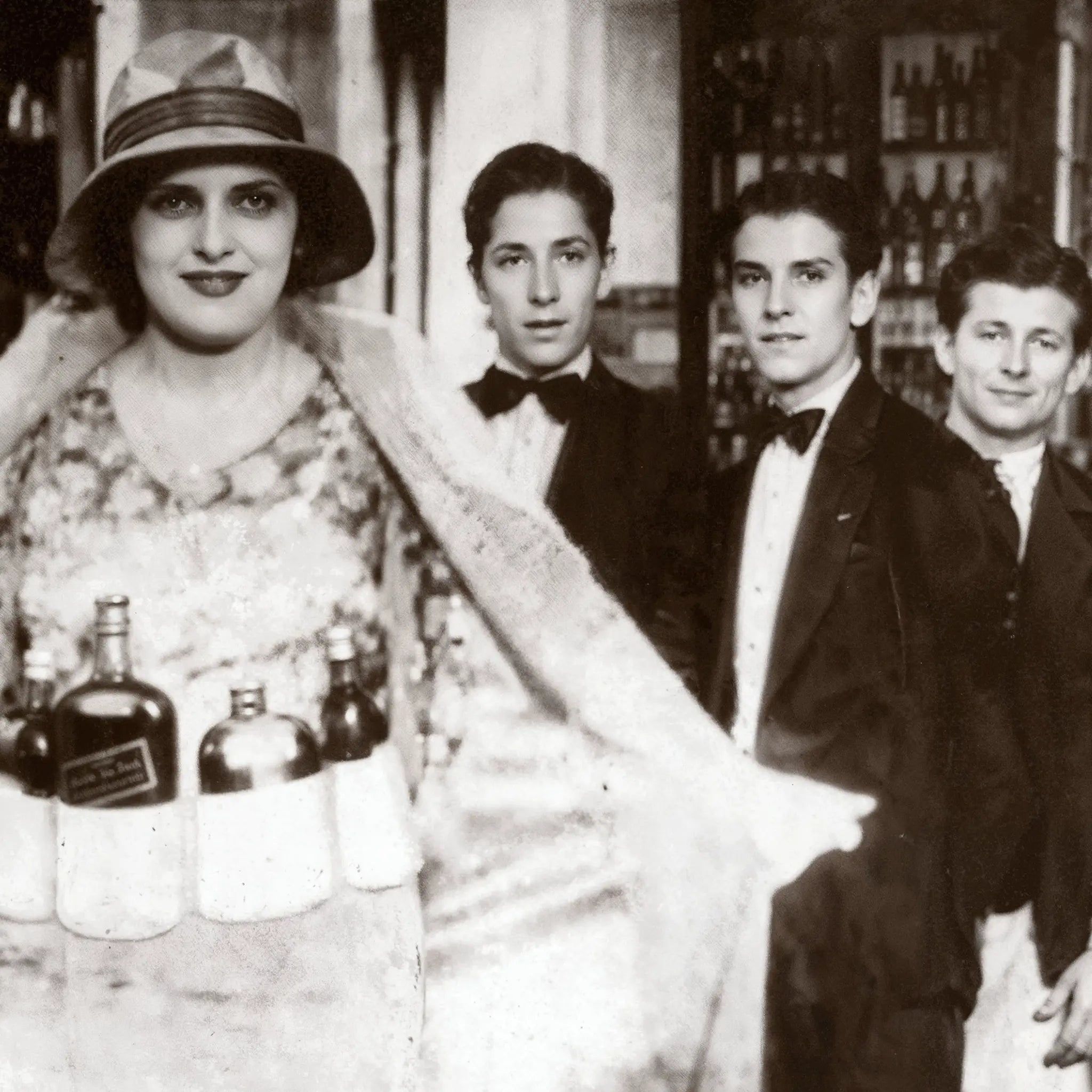 Close-up detail of speakeasy bottle dress showing woman's theatrical costume and formal attire of male patrons