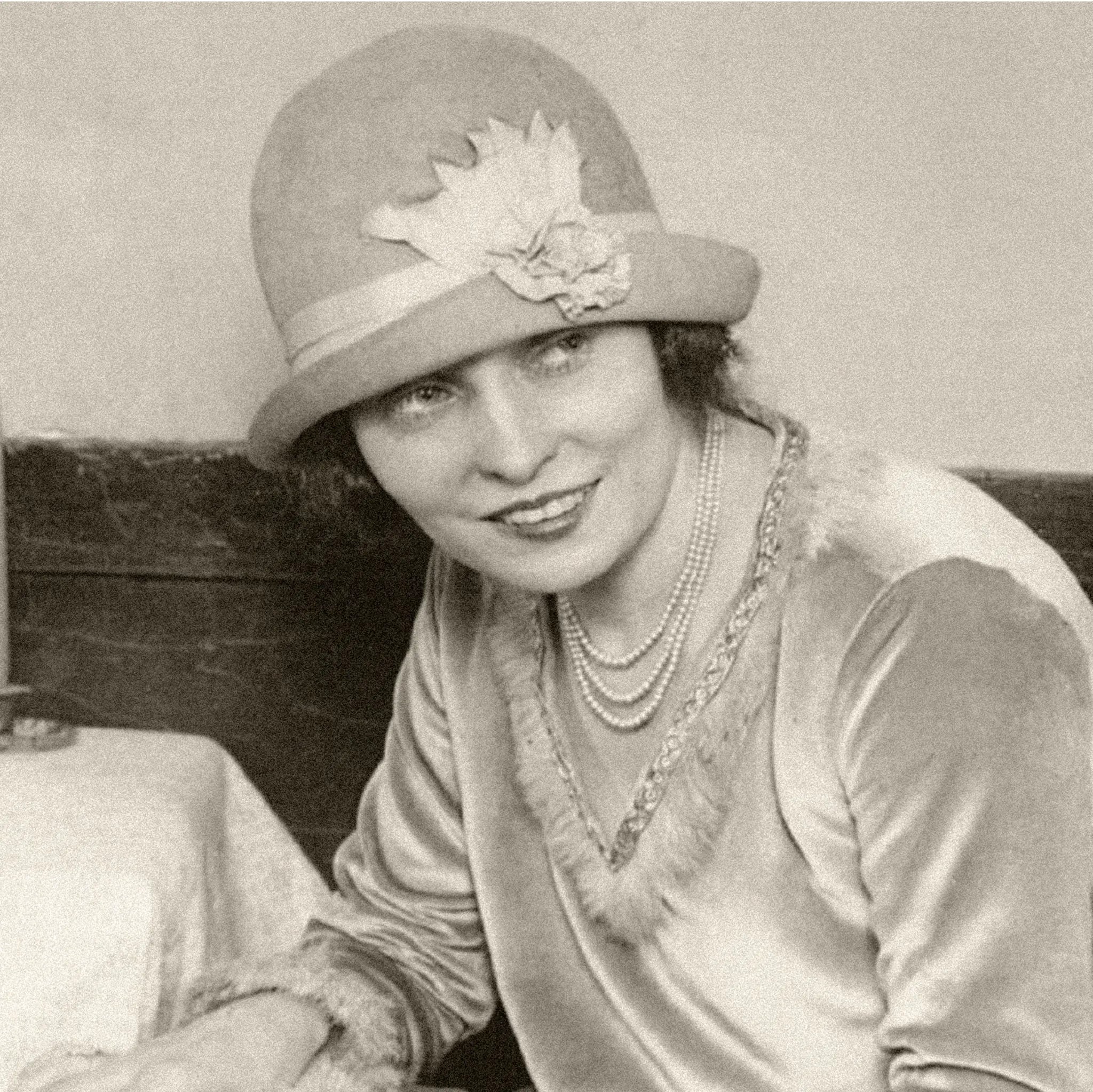 Close-up detail of Jazz Age woman showing elegant cloche hat with flowers and multiple pearl necklaces in sophisticated yacht setting