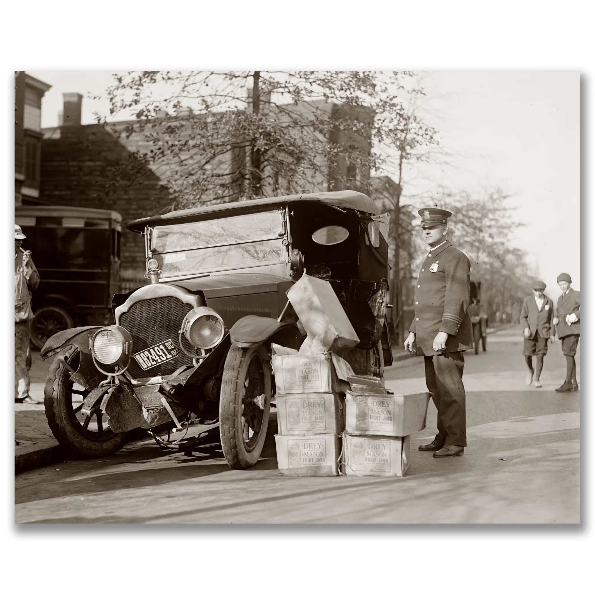 Prohibition era photograph showing police officer with confiscated liquor cases beside vintage automobile during enforcement operation